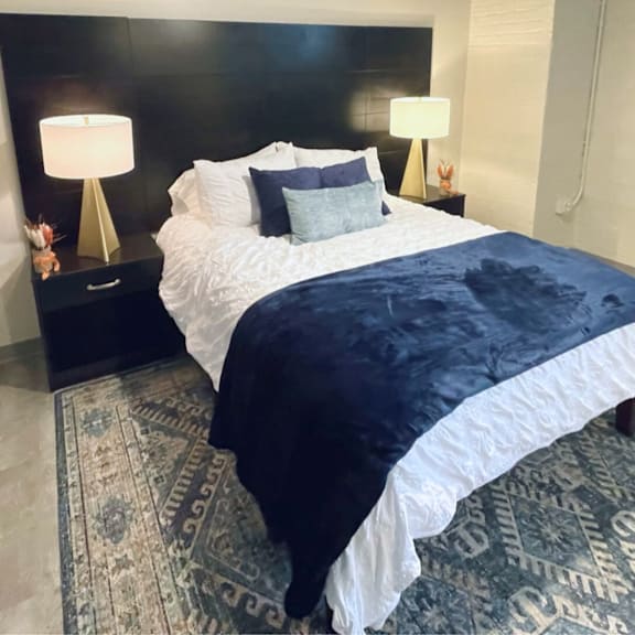 A bed with a white comforter and a blue blanket is in the center of the image.