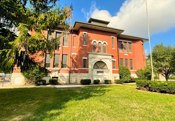 A red building with a white arched entrance sits on a green lawn.