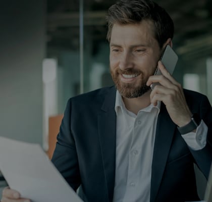 A man in a suit is talking on the phone and holding a document.