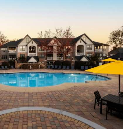 A large outdoor swimming pool surrounded by a brick patio and lounge chairs at The Reserve at Sugarloaf Apartments, Duluth, GA, 30097