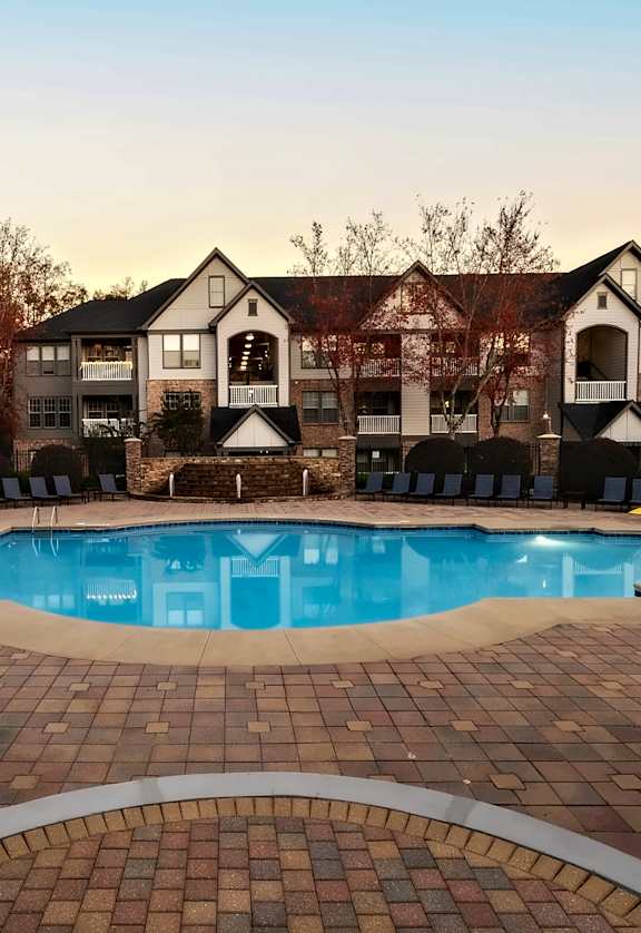 A large outdoor swimming pool surrounded by a brick patio and lounge chairs.