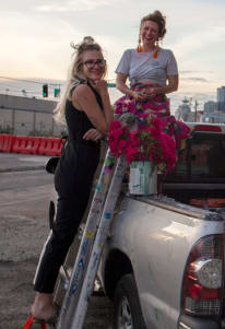 two women standing on a ladder with flowers in the back of a truck