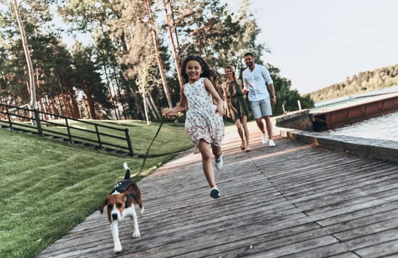 cute little girl running with dog and smiling while her parents walking behind