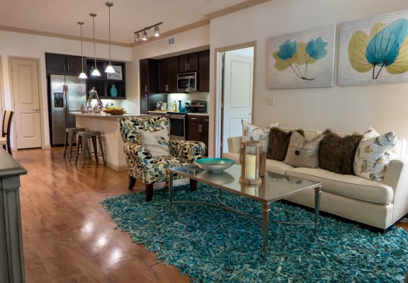 a living room with a couch coffee table and chairs and a kitchen in the background