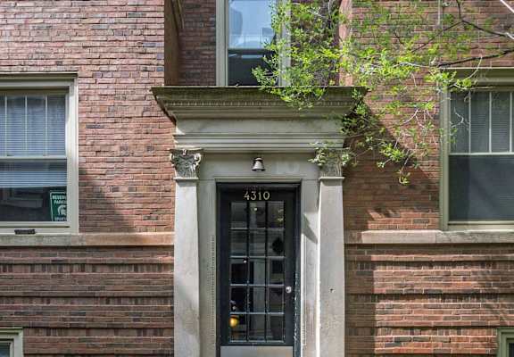 a brick building with a black door and a tree in front of it