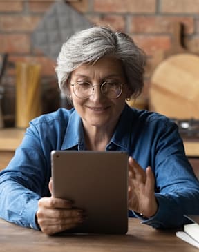 An older woman with glasses is using a tablet.