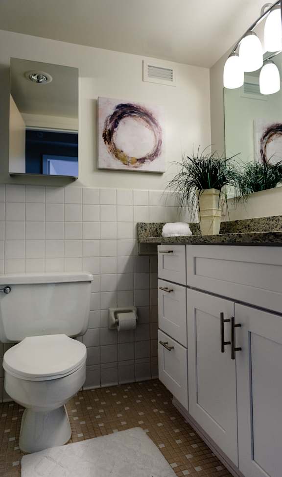 A white toilet sits in a bathroom with a brown and white tiled floor at Hampton Plaza Apartments, Towson, MD, 21286