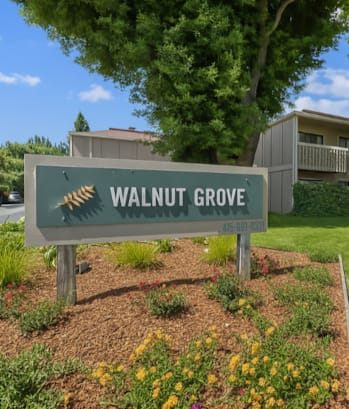 A sign for Walnut Grove stands in front of a building and trees.