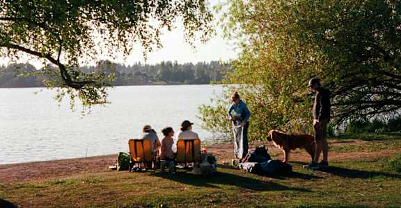 A family of four sitting on a lawn by a lake with a dog.