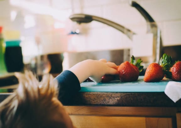 a child reaching for strawberries on a cutting board