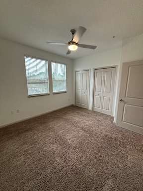 an empty living room with a ceiling fan and two windows