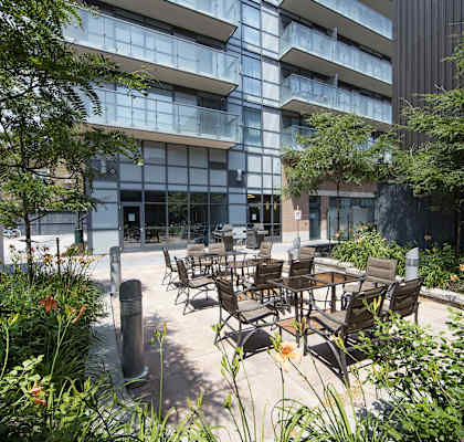 A modern building with a glass facade and a courtyard with tables and chairs.