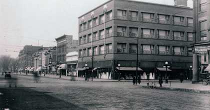 A black and white photo of a street with a large building on the right.