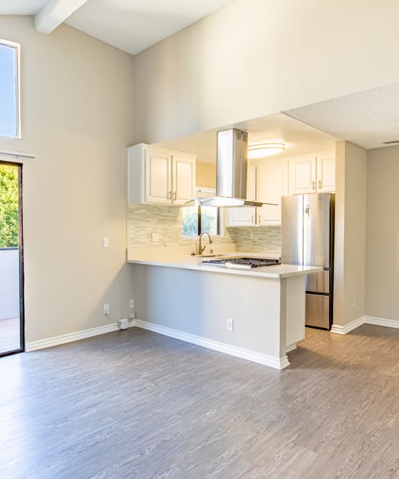 an empty living room with a kitchen and a sliding glass door