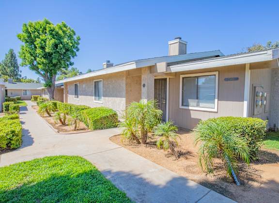 a beige house with a sidewalk and palm trees in front of it