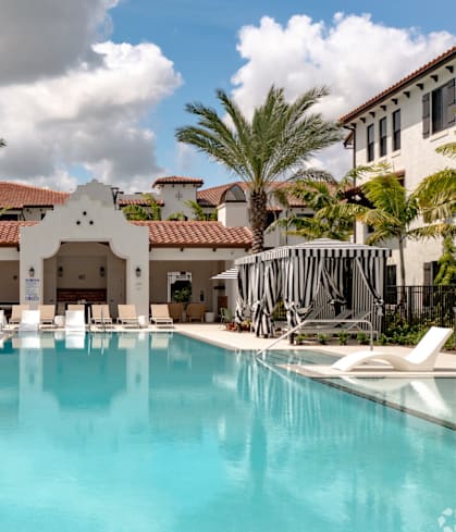 A large swimming pool in front of a building with palm trees.