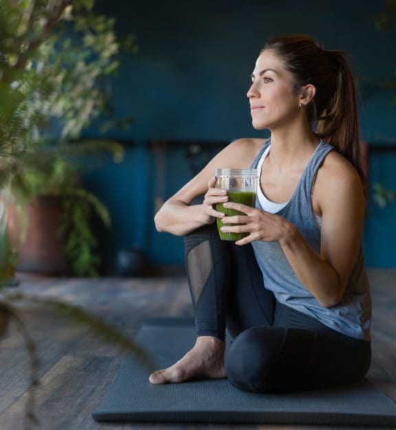 a woman sitting on a yoga mat holding a glass of green juice at VALE Lake Wylie Apartments, Clover , South Carolina