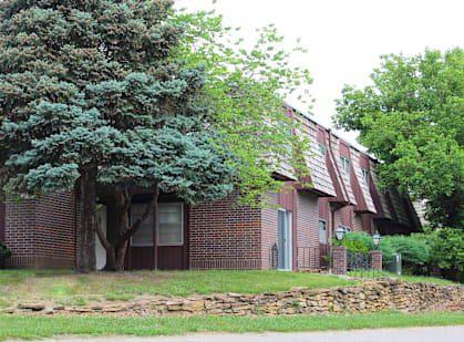 A red brick house with a large tree in front.
