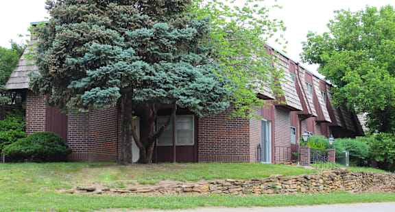 A red brick house with a large tree in front.
