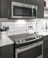 Luxury 2 BR Apartments in Portland OR - Couch9 Apartments - Modern Kitchen with Stainless Steel Appliances, Quartz Countertops, Tile Backsplash, Grey Cabinetry, and Hardwood Flooring