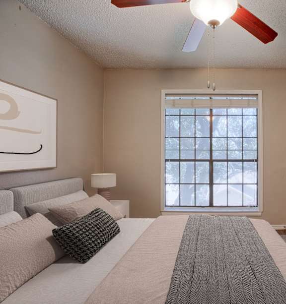 A bedroom with a bed, pillows, a ceiling fan, and a window.