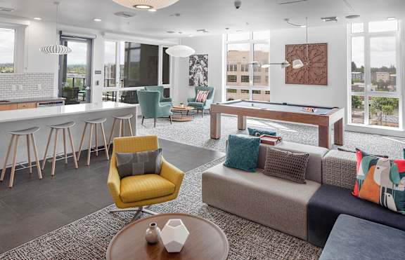 A modern living room with a pool table and a kitchen area.