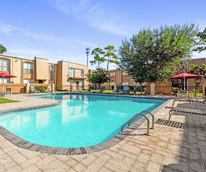 A swimming pool surrounded by a brick patio and apartment buildings.