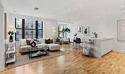 A living room with a white sofa set and a wooden floor.