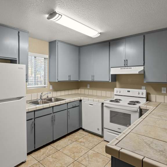 A kitchen with a white refrigerator, white oven, and grey cabinets.at Cedar Park Apartments, Chico, CA, 95926