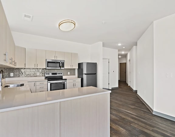 a white kitchen with a large island and a stainless steel refrigerator at Metropolis Apartments in Glen Allen, VA 23060