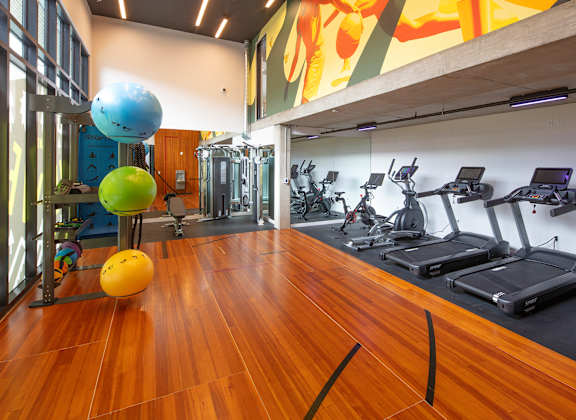 a gym with cardio equipment and weights on a wooden floor at The Weidler in Portland, OR 97209