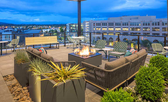 A patio with a fire pit and seating area overlooking a cityscape at dusk.