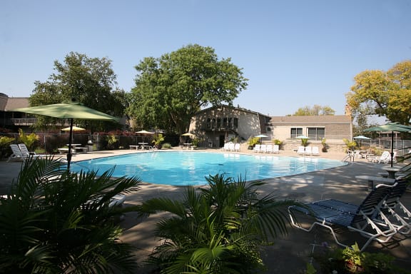 A swimming pool with chairs and a building in the background at Eden West Apartments.
