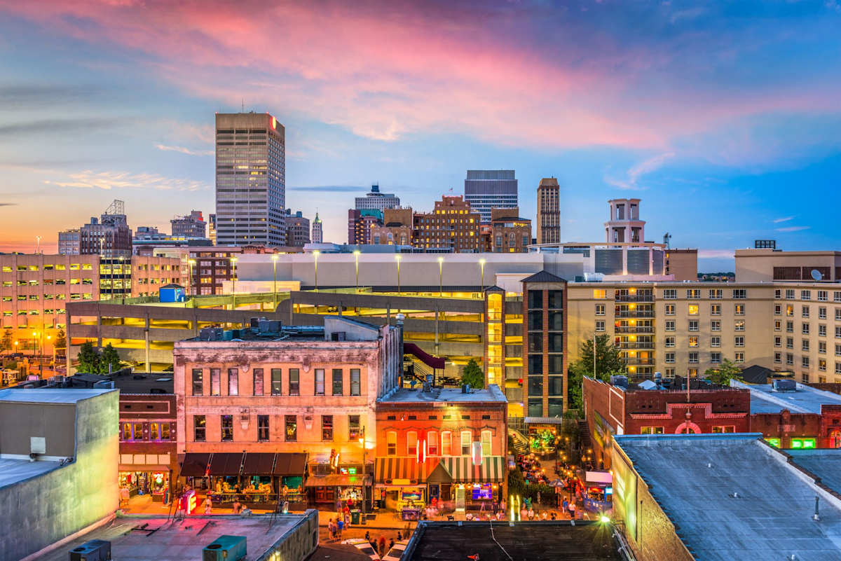 A cityscape at dusk with buildings illuminated and a clear sky.
