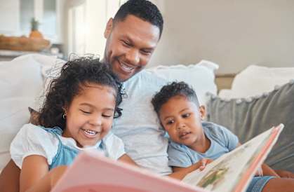 a father reading a book to his daughters on the couch