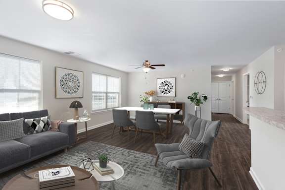 A living room with a grey sofa, a grey armchair, a wooden coffee table, a white dining table, and a ceiling fan.