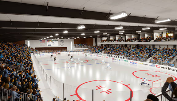 A hockey game is being played in a large arena with a Verizon advertisement on the wall.