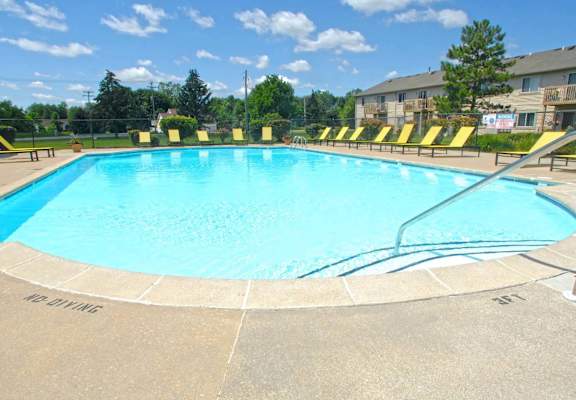 a large pool with yellow chairs around it in front of an apartment building