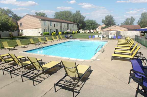 A pool surrounded by chairs in a sunny outdoor setting.