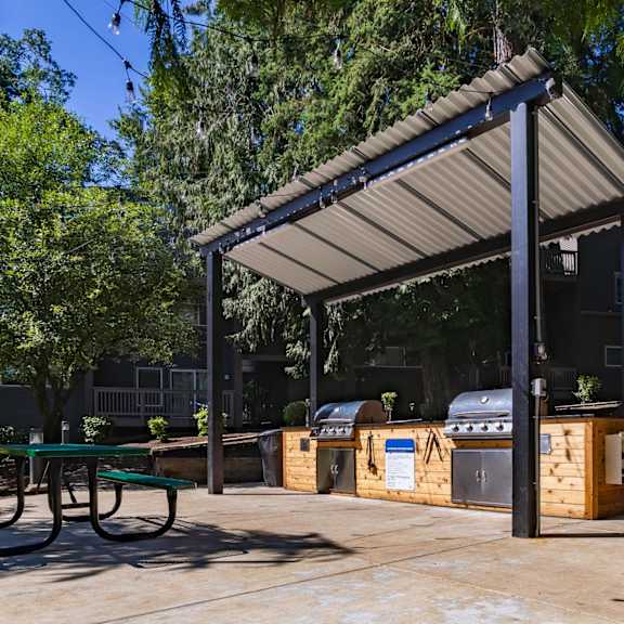 A covered picnic area with a grill and a table.