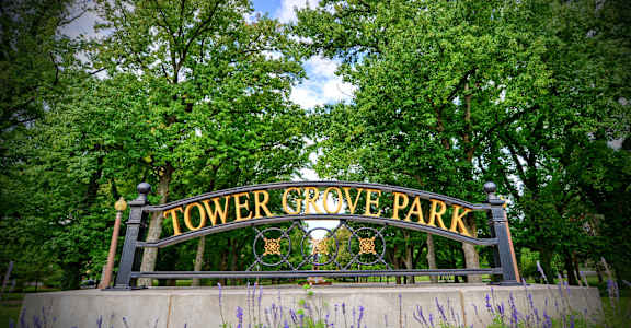 A sign that says "Tower Grove Park" is in front of some trees.