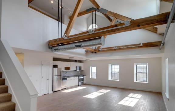 an open living room with a kitchen and exposed beams in the ceiling at Ames Shovel Works Apartments in North Easton, MA 02356