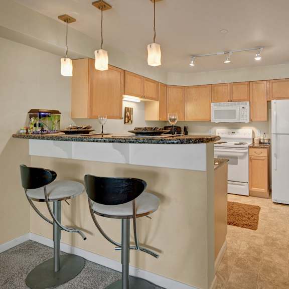 A kitchen with a barstool and chairs Admirals Cove Apartments.
