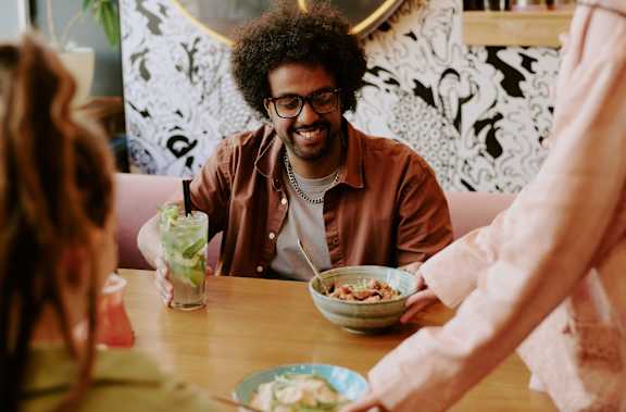 A man with an afro is sitting at a table with a bowl of cereal and a glass of milk.