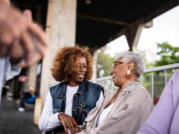 Two people are standing under a structure with a blurred background.