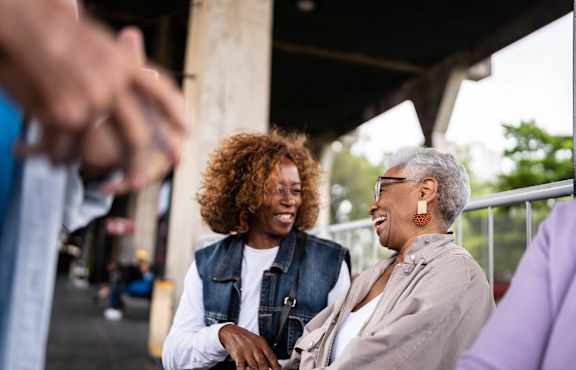 Two people are standing under a structure with a blurred background.