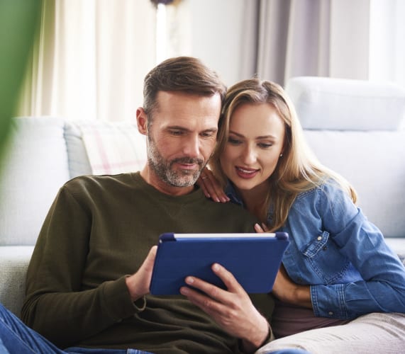 a man and woman sitting on a couch looking at a tablet