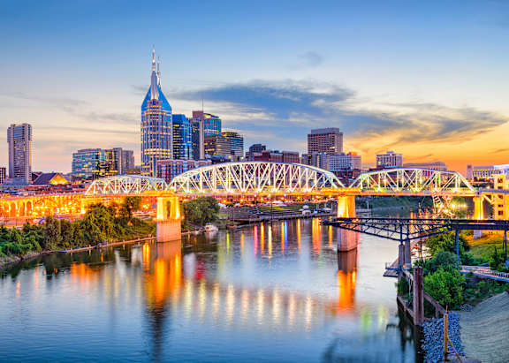 A city skyline is reflected in a lake with a building in the foreground.