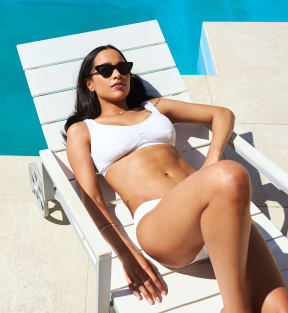 a woman in a white bikini and sunglasses laying on a beach chair at the edge of a at Urban Crest Apartments, San Antonio, TX, 78209