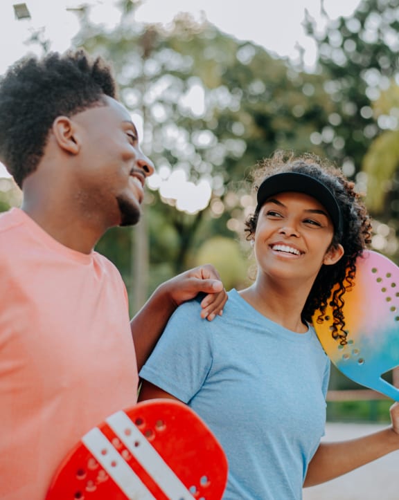 a man and a woman standing in a park holding balloons and tennis rackets
